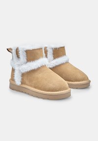 Botas de tobillo de ante marrón con ribete de piel sintética blanca, puntera redondeada y suela de goma plana. Incluye una pestaña en la parte posterior para facilitar el calzado.