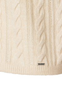 Cremfarbener Kabelstrickpullover mit strukturierten Mustern, geripptem Saum und einem kleinen, silbernen Logosticker am unteren Ende. Aus weichem Wollmaterial.