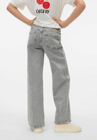 Vaqueros de pierna ancha color gris claro con una superficie texturizada, cinco bolsillos y cintura alta, combinados con zapatos de lona beige.