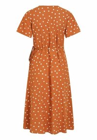 Robe couleur rouille avec des pois blancs, manches courtes, taille cintrée et jupe fluide. Le tissu texturé ajoute de la dimension.