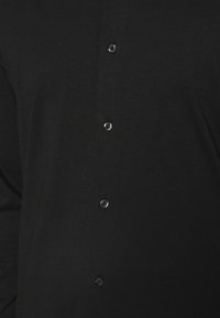 Czarna koszula z gładkim materiałem, zapinana na przód na sześć błyszczących czarnych guzików, bez widocznych wzorów ani grafik.