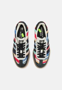 Paire de baskets Adidas en tissu rayé multicolore, lacets noirs, bout beige et semelles intérieures de marque, vues de dessus sur fond blanc.