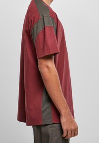 Camiseta de manga corta color granate con un panel lateral en gris oscuro contrastante, hecha de algodón suave, con un ajuste relajado y detalles de costura simple.