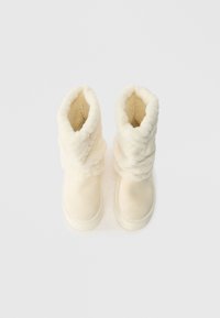 Kremlim krāsas potīšu zābaki ar mīkstu, strukturētu kažokādas oderi un gludu ārējo materiālu. Augšdaļai ir salocīts dizains papildu siltumam.