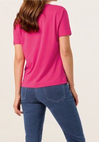 Lyserød bomulds T-shirt med kortærmer, rund halsudskæring og afslappet pasform, parret med blå denimjeans med baglommer.