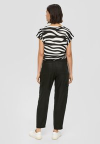 Zwart-wit gestreepte top met korte mouwen, gecombineerd met zwarte cargobroek. Lichtgewicht, relaxed fit, zichtbare zakken op de broek. Witte sneakers.