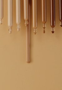 Un ensemble de tubes allongés et cylindriques dans des nuances de beige à marron, avec des surfaces brillantes et des extrémités arrondies, suspendus sur un fond beige.