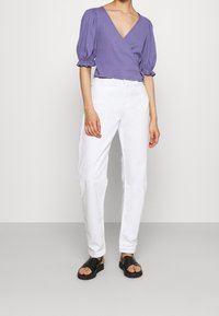 Top envolvente morado de manga corta con escote en V profundo, combinado con pantalones blancos de cintura alta y sandalias negras. Diseño simple, corte casual.