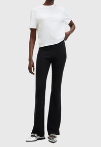 Bílý zkrácený tričko s krátkými rukávy, doplněné černými rozšířenými kalhotami a plochými stříbrnými botami. Hladká tkanina a přiléhavý design.