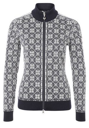 Kvinde går iført en sort-hvid mønstret lynlåsjakke, grå T-shirt, revnede hvide bukser og sorte vandrestøvler.