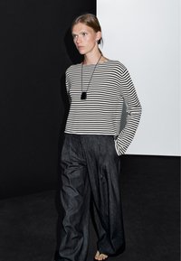 Gestreepte lange mouw top in zwart en wit, gecombineerd met loszittende donkere denim broek. Bevat een cirkelvormige ketting als accent.
