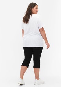 Camiseta blanca de algodón con mangas cortas, combinada con pantalones capri negros a la altura de la rodilla y zapatillas blancas. Diseño sencillo, textura suave.