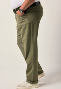 Pantalones verde oliva de mezcla de algodón, con piernas rectas, bolsillos laterales y dobladillo ajustado, combinados con zapatillas blancas.