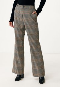 Checkered trousers in black, white, and orange tones. High-waisted with flared legs, pockets, and a button closure. Smooth fabric texture.
