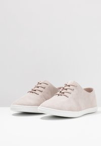 Zapatos beige de ante con cordones, de textura suave, suela de goma blanca y diseño minimalista. Presentan costuras sutiles y una forma de punta redondeada.