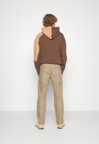 Brun och tan färgblockerad hoodie med huva, tillsammans med beige cargobyxor med sidofickor och avslappnad passform.