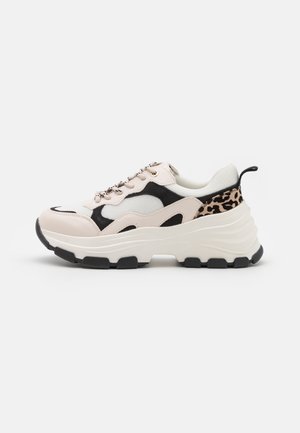 Kraftig sneaker med beige, sorte og hvide paneler, leopardprint detaljer, tyk hvid sål og sort mønster, vist fra siden.