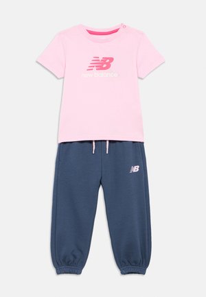 T-shirt de manga curta rosa da New Balance com logótipo, combinado com calças de jogging azul-marinho com cordão, apresentando punhos elásticos e logótipo.