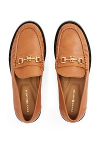 Tan leather loafers feature a gold chain accent, rounded toe, stitched detailing, and a patterned insole. Rubber sole for grip.