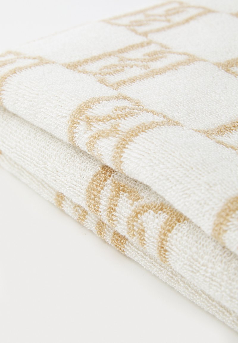 Asciugamano bianco con motivo a righe beige, piegato con una superficie texturizzata, caratterizzato da accenti decorativi in un design geometrico.