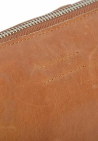 Billetera de cuero marrón claro con costuras visibles y un zipper plateado. La textura es suave con ligeras imperfecciones y un brillo sutil.