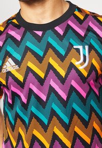 Adidas-tröja med svart bas, som har ett livligt zigzag-mönster i rosa, teal, orange och lila. Inkluderar vita logotypaccenter.