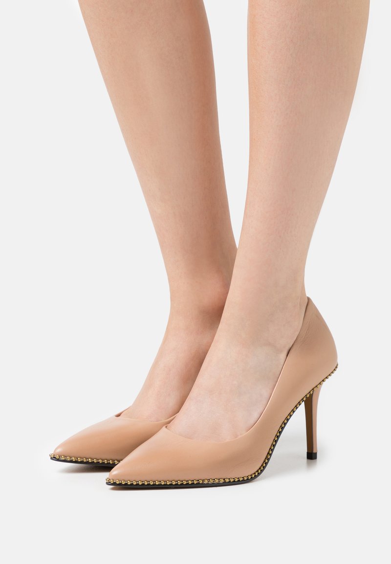 Pumps nude in pelle con tacco alto, punta affusolata e dettagli in perline dorate lungo la suola. Design elegante con una texture liscia.