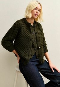 Donkergroene gebreide cardigan met een gestructureerd ruitpatroon, ronde halslijn, knoopsluiting en geribde manchetten. Draag het over donkerdenim jeans.