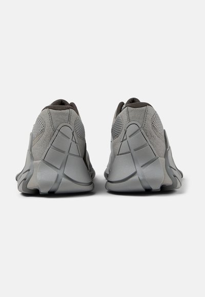 Gray athletic shoes with a textured upper, mesh panels, and distinctive sculpted sole design. Features padded collar and heel accents.