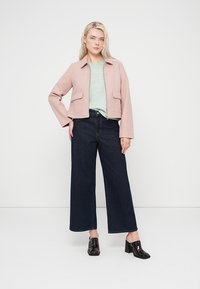 Φωτεινό ροζ cropped σακάκι με δύο μπροστινές τσέπες, συνδυασμένο με τοπ σε μέντα πράσινο και σκούρο τζιν φαρδιάς γραμμής. Το μοντέλο φοράει μαύρα παπούτσια με τακούνι.