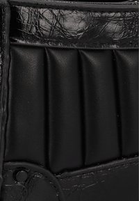 Accessorio in pelle nera con una finitura testurizzata e stropicciata, dotato di pieghe verticali e dettaglio a rivetto circolare sul lato.