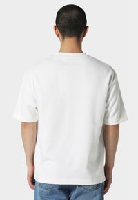 Hvit kortermet t-skjorte med avslappet passform, rund hals og glatt tekstur, kombinert med blå jeans.