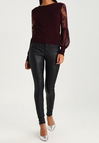 Bordruim gebreid trui met doorzichtige kantmouwen, zwarte nep leren broek en zilveren puntige hakken. Strakke en aansluitende ontwerp.