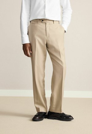 Beige dress pants with a flat front, straight leg design, featuring side pockets and a button closure, paired with shiny black shoes.