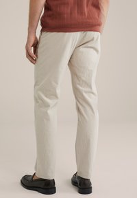 Pantalones de sastrería en un beige claro con un acabado texturizado, con corte recto y bolsillos laterales, combinados con zapatos negros de tipo mocasín.
