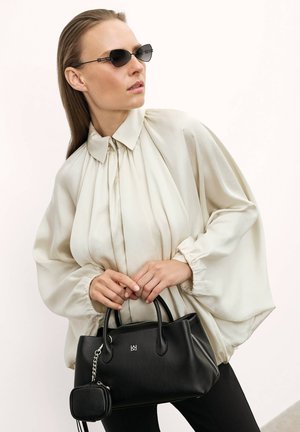 Zwarte leren handtas met zilveren rits en logo, gecombineerd met een crèmekleurige zijden blouse met plooien en luchtige mouwen.