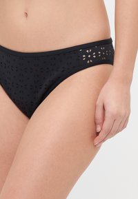 Bas de bikini noir avec un design découpé et des motifs floraux le long de la taille, fabriqué en tissu lisse avec une texture douce.