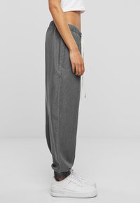 Gray high-waisted joggers in lightweight fabric, featuring an elastic waistband with drawstring, side pockets, and cuffed ankles.
