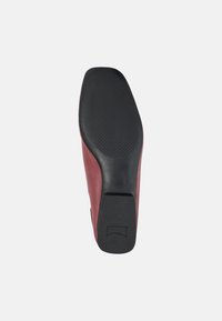 Suela de zapato con un fondo de goma negra texturizada y un lado de cuero burdeos liso. Presenta una forma redondeada y un diseño de tacón bajo.
