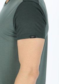 Mørke teal kortærmet t-shirt med en glat tekstur og en kontrasterende lys grøn overdel. Har et lille logo mærke på ærmet.