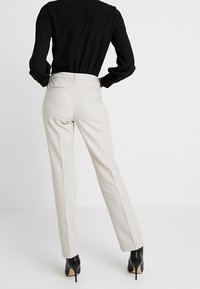 Beige-housut, jotka on räätälöity suoraan istuviksi, varustettu takataskuilla, käytetään mustan istuvan paidan ja mustien korkokenkien kanssa. Suora pinta.