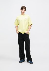 Ανοιχτό κίτρινο oversized t-shirt, μαύρο παντελόνι σε γραμμή wide-leg και μπλε αθλητικά παπούτσια με τρεις ρίγες. Απλός σχεδιασμός, αναπνεύσιμο ύφασμα, άνετη εφαρμογή.