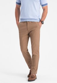Chinos beige à coupe slim, avec poches avant, texture lisse et conception légère, associés à des mocassins en daim marron.