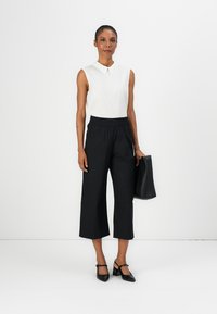 Blusa bianca senza maniche con colletto, abbinata a pantaloni neri a gamba larga e tacchi a punta neri. Porta una borsa nera.