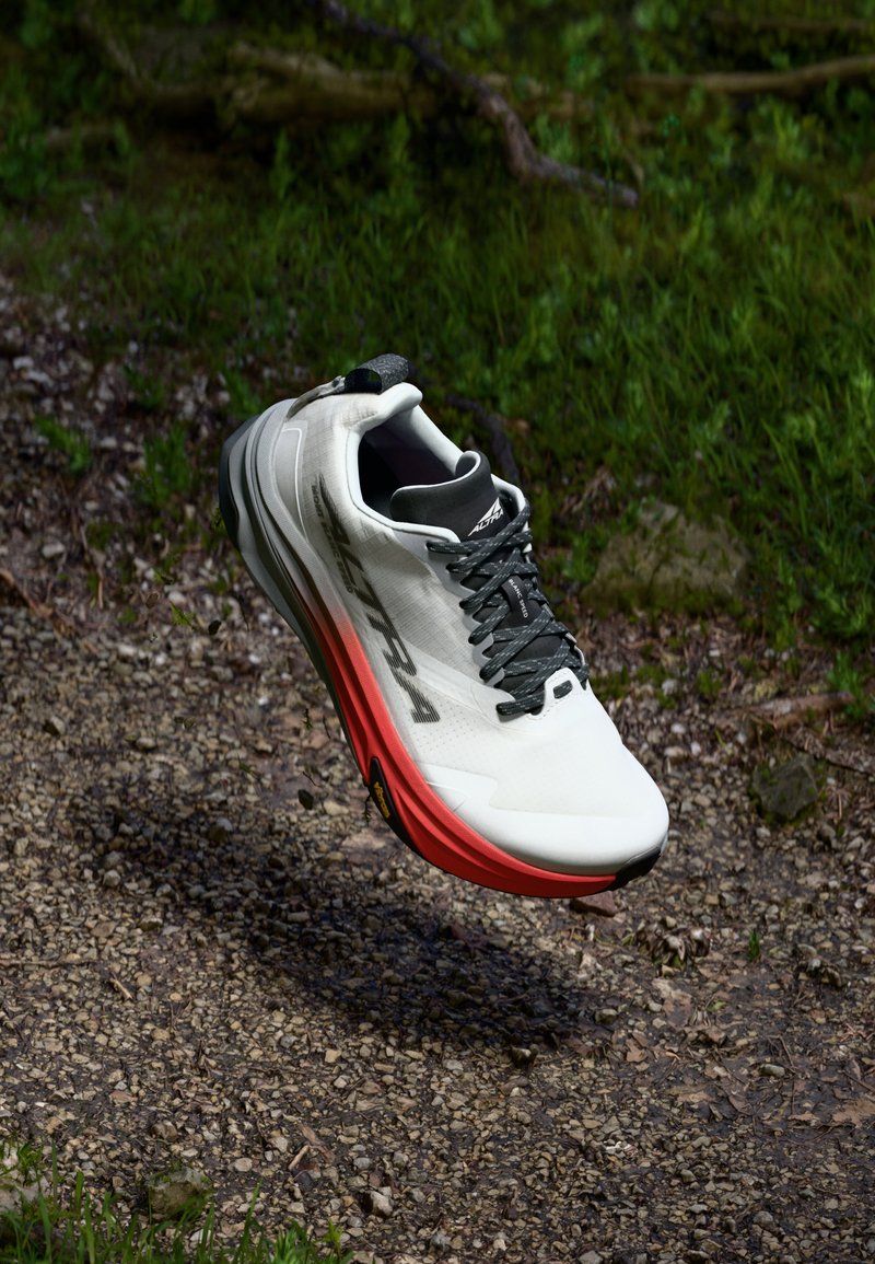 Chaussure de course légère en blanc et rouge, avec un dessus texturé, des lacets noirs et une semelle rembourrée pour un confort et une adhérence accrus.