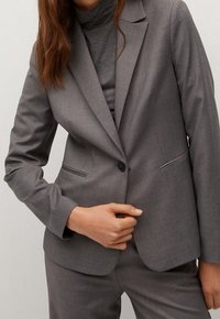 Grijze op maat gemaakte blazer met een enkele knoopsluiting, notch revers, twee voorzakken en een subtiele textuur. Draagt over een bijpassend fitted top.