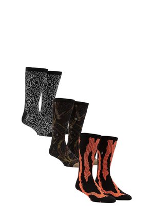 Quatre paires de chaussettes : noires avec un motif abstrait blanc, noires avec des accents marron, et noires avec un design en flammes orange, toutes tricotées.