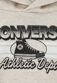 Μπεζ φούτερ με κουκούλα που διαθέτει γραφικό μαύρου παπουτσιού Converse, έντονο κείμενο με τις λέξεις "CONVERSE" και "Athletic Dept." και λευκές οριζόντιες ρίγες.