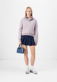 Lilac zip-up sweatshirt, navy pleated skirt, blue handbag, white socks, and silver shoes. Simple design with contrasting colors and textures.