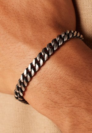 Black and silver metal chain bracelet with interlocking links, showing a smooth and shiny texture against a tanned skin tone.